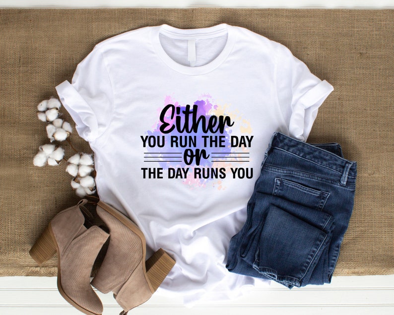 K&ouml;nnte beinhalten: Wei&szlig;es T-Shirt mit Aquarellhintergrund und dem Text "Either you run the day or the day runs you".