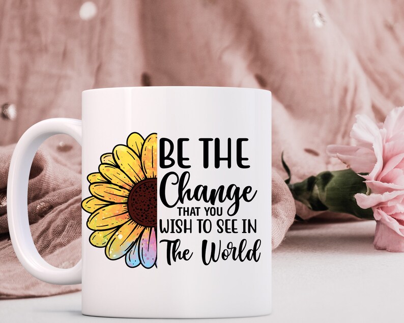 K&ouml;nnte beinhalten: Wei&szlig;e Keramiktasse mit einer schwarz-wei&szlig;en Grafik einer Sonnenblume und dem Text "Sei die Ver&auml;nderung, die du in der Welt sehen m&ouml;chtest".