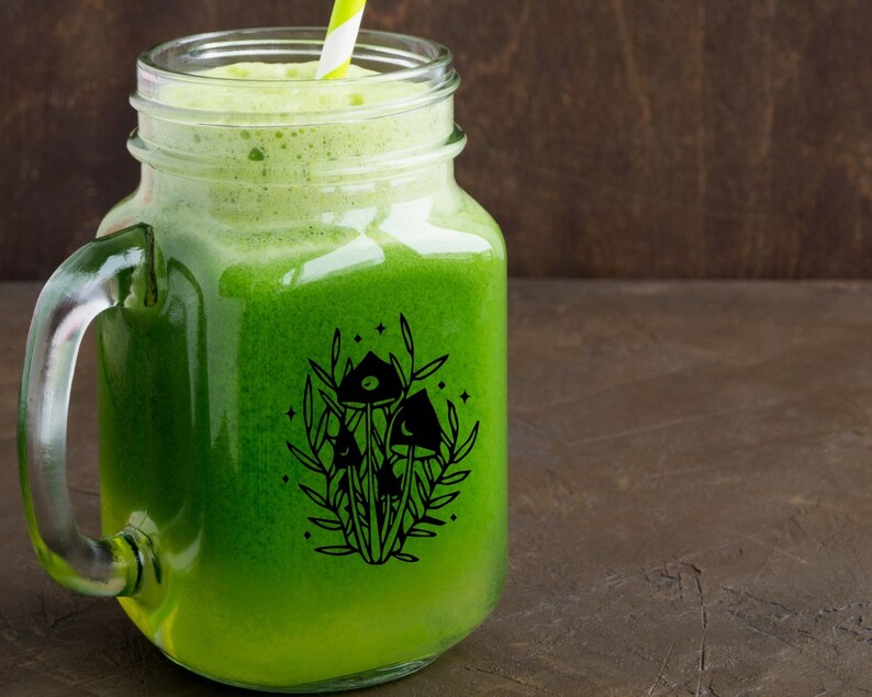 May include: A mason jar filled with green juice and a black and white illustration of mushrooms and stars on the side.