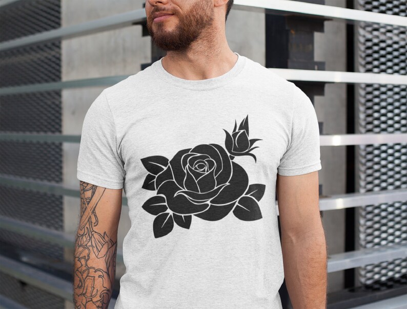 May include: A light gray t-shirt featuring a large black rose design. The graphic includes a fully bloomed rose, a bud, and several leaves. The shirt is made of a soft material.