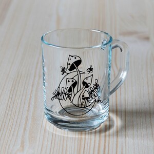 May include: A clear glass mug with a black and white design of mushrooms and leaves.