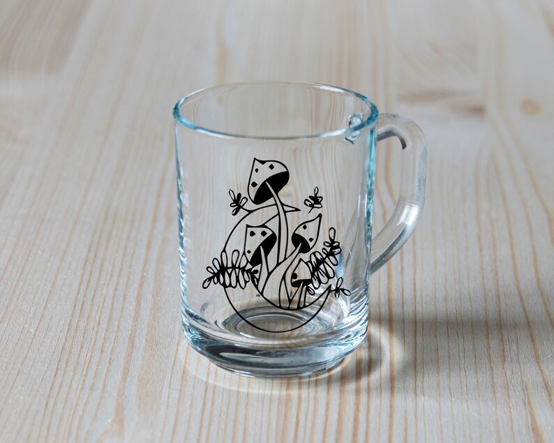 May include: A clear glass mug with a black and white design of mushrooms and leaves.