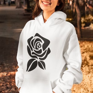 May include: White hoodie with a black rose graphic. The hoodie has a front pocket and a hood. The rose design is a simple, stylized illustration. The person is wearing the hoodie outdoors.