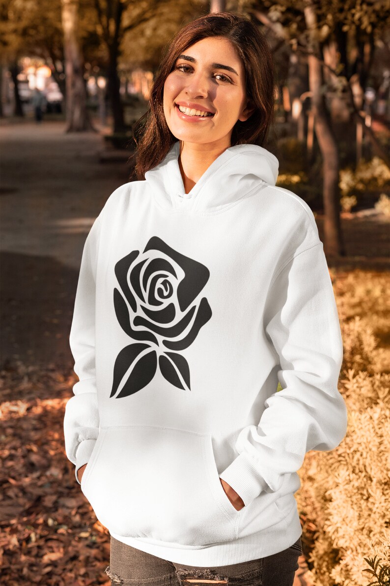 May include: White hoodie with a black rose graphic. The hoodie has a front pocket and a hood. The rose design is a simple, stylized illustration. The person is wearing the hoodie outdoors.