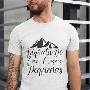 Op de afbeelding: Een lichtgrijs t-shirt met een zwart bergmotief en de Spaanse tekst "Disfruta De Las Cosas Peque&ntilde;as". Het shirt is gemaakt van een zacht materiaal.