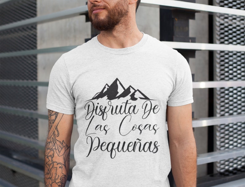 Op de afbeelding: Een lichtgrijs t-shirt met een zwart bergmotief en de Spaanse tekst "Disfruta De Las Cosas Peque&ntilde;as". Het shirt is gemaakt van een zacht materiaal.