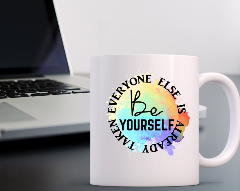 K&ouml;nnte beinhalten: Wei&szlig;e Keramik-Kaffeetasse mit einem farbenfrohen Aquarelldesign und dem Text "Be Yourself Everyone Else Is Already Taken".
