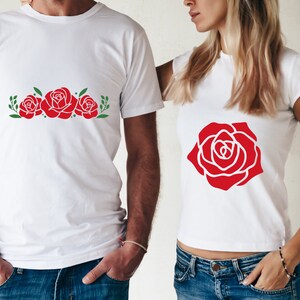 K&ouml;nnte beinhalten: Wei&szlig;e T-Shirts mit roten Rosenmustern. Ein Shirt zeigt drei Rosen mit gr&uuml;nen Bl&auml;ttern, das andere eine einzelne gro&szlig;e Rose. Die Shirts sind kurz&auml;rmlig und f&uuml;r Freizeitkleidung geeignet.