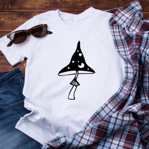 May include: White t-shirt with a black and white illustration of a mushroom with stars and moons on the cap.