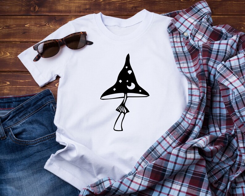 May include: White t-shirt with a black and white illustration of a mushroom with stars and moons on the cap.