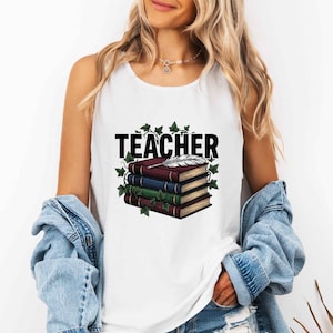 May include: A white sleeveless tank top featuring a graphic print of a stack of three books in maroon, blue, and green. A white feather quill rests on top of the books, surrounded by green ivy leaves. The word TEACHER is printed in bold black letters.