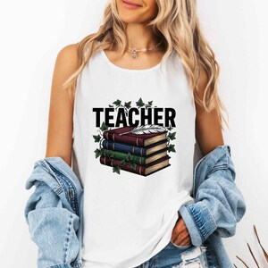 Pode incluir: Uma regata branca sem mangas com uma estampa gráfica de uma pilha de três livros em bordô, azul e verde. Uma pena branca repousa sobre os livros, cercada por folhas de hera verdes. A palavra TEACHER está impressa em letras pretas.