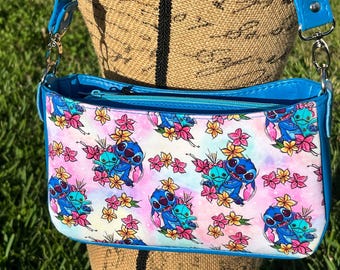 May include: A blue and white shoulder bag with a zipper closure. The bag features a repeating pattern of Stitch from Lilo & Stitch holding a flower.