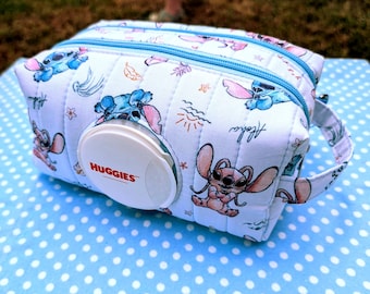 May include: A light blue quilted fabric wipe dispenser case featuring a repeating pattern of the character Stitch, tropical leaves, and the word Aloha. The case includes a white plastic Huggies brand flip-top lid and a side carrying handle.