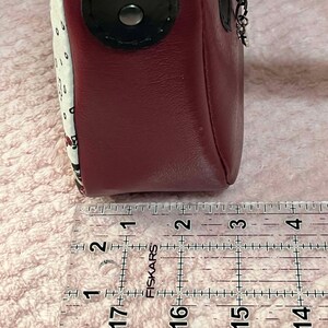 Puede incluir: Primer plano de un bolso de cuero rojo con un patr&oacute;n de lunares blancos y negros. El bolso se mide con una regla, mostrando que tiene aproximadamente 7,6 cm de ancho.