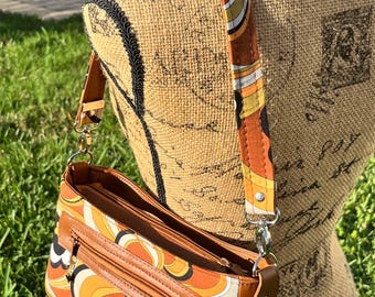 May include: A brown and orange shoulder bag with a retro swirl pattern. The bag has a brown leather trim and a zipper closure. The shoulder strap is adjustable and has a brown and white swirl pattern.