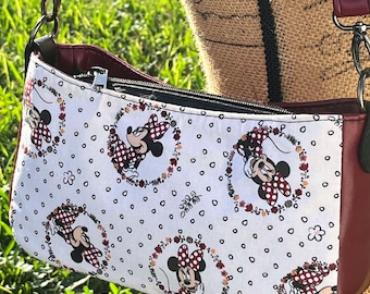 May include: A red and white crossbody bag with a Minnie Mouse print. The bag has a zipper closure and a long adjustable strap.
