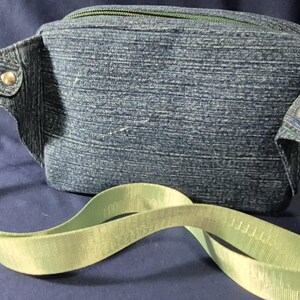 May include: A denim fanny pack with a light green strap and gold-colored hardware. The fanny pack has a zipper closure and is made of a blue denim material. The strap is adjustable and has a buckle closure. The bag is designed to be worn around the waist or across the body.
