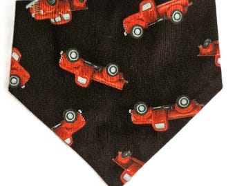 May include: A black bandana with a repeating pattern of red vintage pickup trucks. The trucks have white tires and are arranged in various orientations across the fabric. The bandana is triangular in shape.