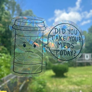 Puede incluir: Una pegatina holográfica con una botella de píldoras de dibujos animados con una cara triste y un globo de diálogo que dice "¿Tomaste tus medicamentos hoy?"