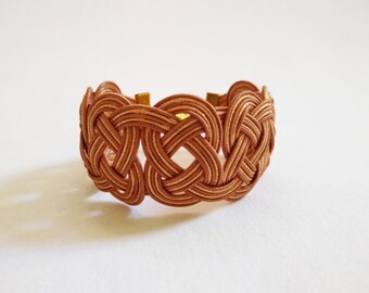 May include: A woven leather bracelet with a knotted design in a light brown color.