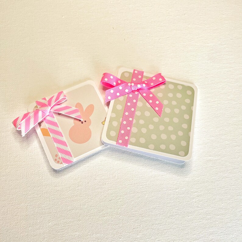 May include: Two square gift boxes with pink ribbons. One box has a light green background with white polka dots. The other box has a bunny graphic and pink and white striped ribbon.