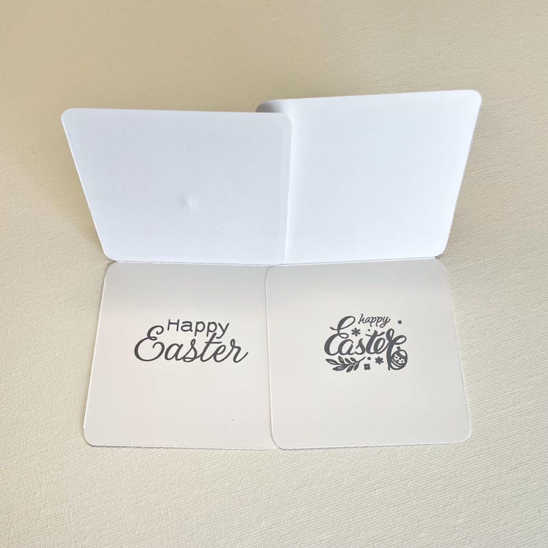May include: White Easter greeting card with the words "Happy Easter" in black script. The card is open, revealing the inside. One side has the words "Happy Easter" and the other side has the words "happy Easter" with floral accents.