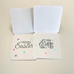 May include: Two square Easter cards with the words "Happy Easter" in black script. One card has a simple font, the other has a decorative font. Both cards have colorful bunny and confetti accents. The cards are open, revealing blank white interiors.