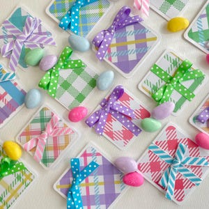 May include: Arrangement of colorful Easter-themed gift tags with plaid patterns and ribbon bows in various colors, including blue, green, and purple. Pastel-colored candy eggs are scattered around the tags, creating a festive and cheerful display.