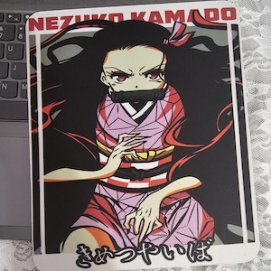 Puede incluir: Alfombrilla de ratón rectangular con un personaje de anime, Nezuko Kamado, con el texto "NEZUKO KAMADO" en la parte superior. El personaje está representado con un kimono rosa con cabello negro y ojos rojos. Texto japonés en la parte inferior.