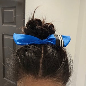 May include: A blue hair bow with white stripes tied in a bow on a person's hair.