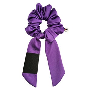 May include: Purple scrunchie with a black band and long tails. The scrunchie is made of a soft, silky fabric.