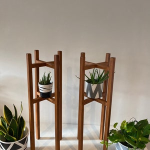 May include: Two wooden plant stands with a geometric design. Each stand has a potted plant with a black and white patterned pot.