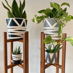 May include: Two wooden plant stands with three shelves each. The top shelves hold potted plants with black and white geometric patterns. The middle shelves hold smaller potted plants with gray and white geometric patterns.
