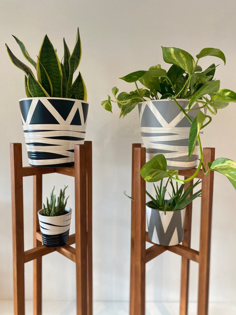 May include: Two wooden plant stands with three shelves each. The top shelves hold potted plants with black and white geometric patterns. The middle shelves hold smaller potted plants with gray and white geometric patterns.