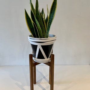 May include: A potted snake plant with green and yellow leaves sits on a wooden plant stand. The pot is black and white with a geometric pattern.