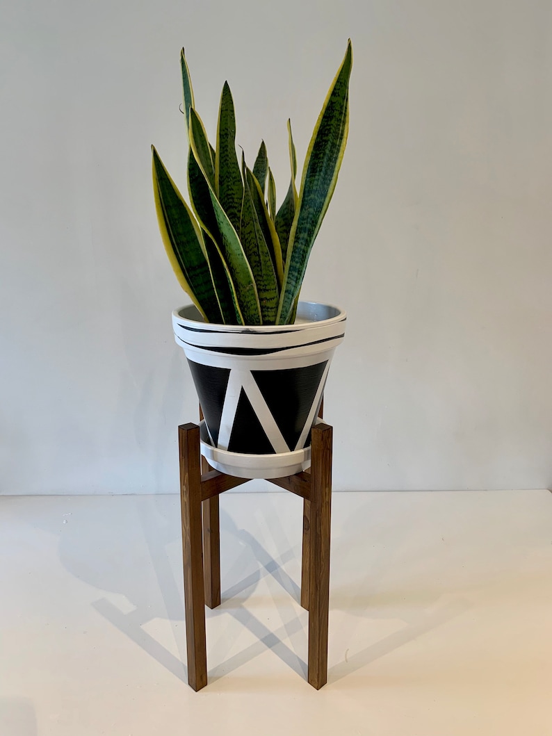 May include: A potted snake plant with green and yellow leaves sits on a wooden plant stand. The pot is black and white with a geometric pattern.