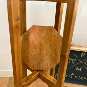 May include: A wooden plant stand with an octagonal top shelf. The stand has a natural wood finish and is made of sturdy wood.