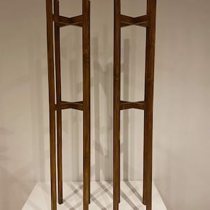 May include: Two wooden plant stands with a dark brown stain. Each stand has three shelves and is made of four vertical pieces of wood.