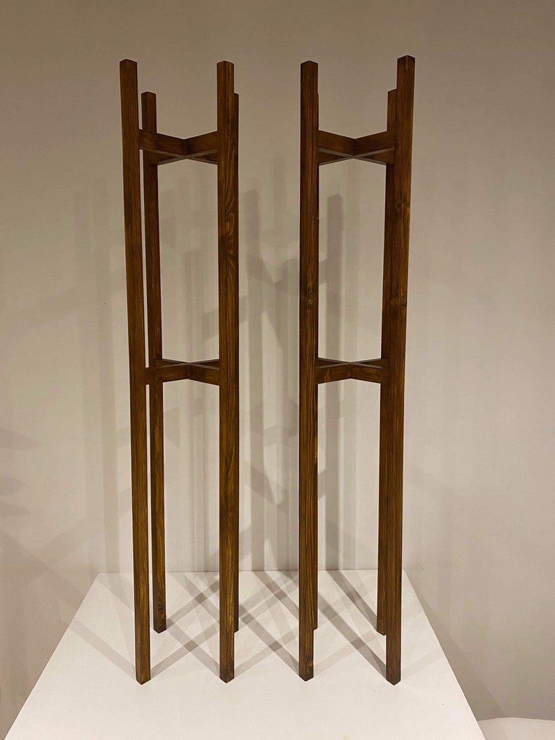 May include: Two wooden plant stands with a dark brown stain. Each stand has three shelves and is made of four vertical pieces of wood.