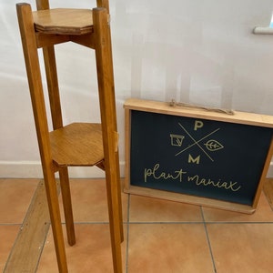 May include: A two-tiered wooden plant stand with a hexagonal top and bottom. The stand is made of natural wood and has a rustic finish. The stand is tall and slender, with four legs.