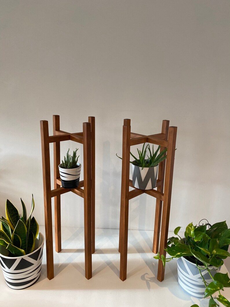 May include: Two wooden plant stands with a geometric design. Each stand has a potted plant with a black and white patterned pot.