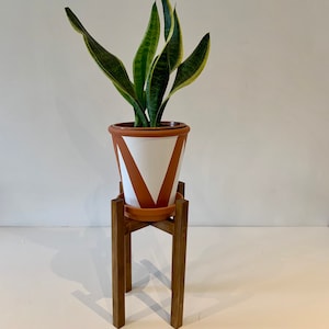 May include: A potted snake plant with variegated leaves sits on a wooden plant stand. The pot is terracotta with white geometric designs.