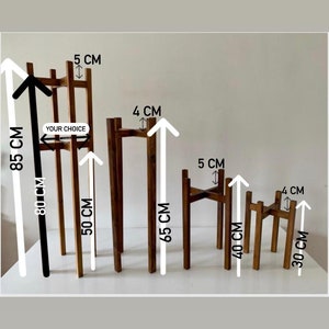 May include: Five wooden plant stands in different sizes. The stands are made of natural wood and have a simple, minimalist design. The stands are 30 cm, 40 cm, 50 cm, 65 cm, and 85 cm tall. The stands are 4 cm and 5 cm wide. The text "YOUR CHOICE" is written on the largest stand.