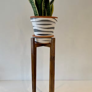 May include: A potted snake plant with green and yellow leaves sits on a wooden plant stand. The pot is white with black stripes.
