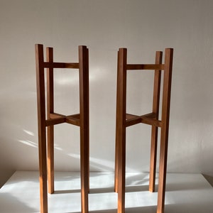 May include: Two wooden plant stands with a simple, rectangular design. The stands are made of natural wood and have a rustic, farmhouse style.
