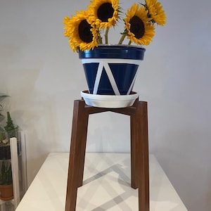 May include: A blue and white ceramic planter with a geometric design sits on a wooden plant stand. The planter is filled with yellow sunflowers.