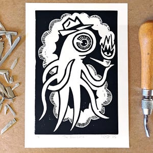 May include: A black and white linocut print titled "The Fell Cuttlefish" featuring an octopus-like creature wearing a hat and smoking a pipe. A carving tool and linoleum scraps are next to the print. The print is on a white background.