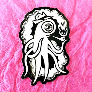 May include: A black and white sticker featuring an octopus-like creature wearing a hat and smoking a pipe. The creature has a large eye and is holding a flame. The sticker is on a pink, textured background.