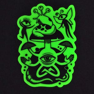 Puede incluir: Una pegatina verde neón con una ilustración negra de una seta y otros elementos psicodélicos. El diseño incluye ojos, manos y una figura de gusano, todos delineados en negro sobre un fondo verde brillante. La pegatina está sobre un fondo negro.
